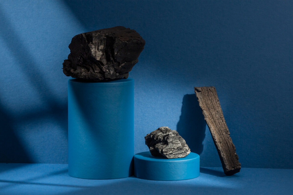 Three dark porous stones arranged on blue cylindrical pedestals against a deep blue background, highlighting texture and structure relevant to choosing the best air stones for hydroponics. Dramatic lighting casts strong shadows, emphasizing the rough surfaces and natural shapes that affect airflow and diffusion in hydroponic systems
